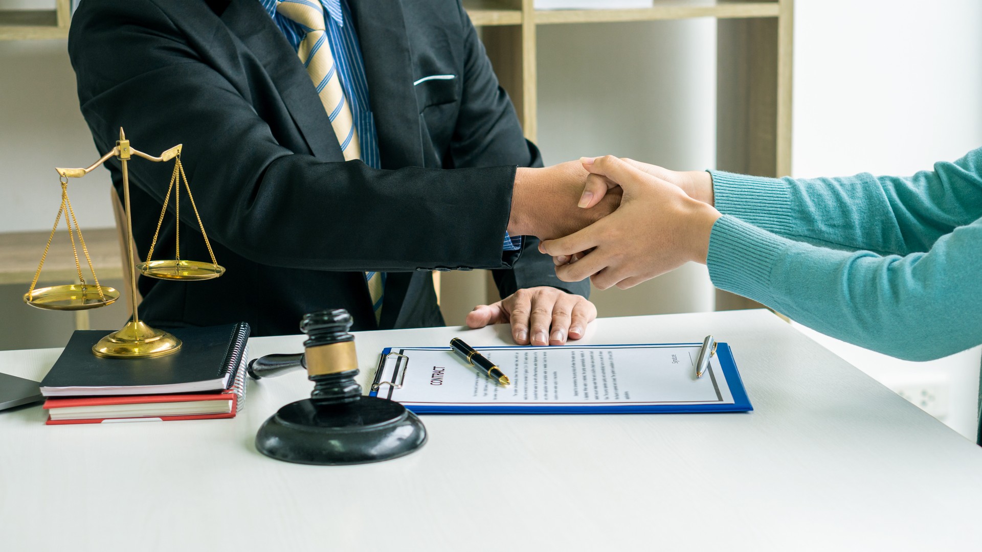 Male lawyer shakes hands with client in close-up office . Banner design lawyer is shaking hands with client about successful resolution of case on table of papers and hammer and golden scales.